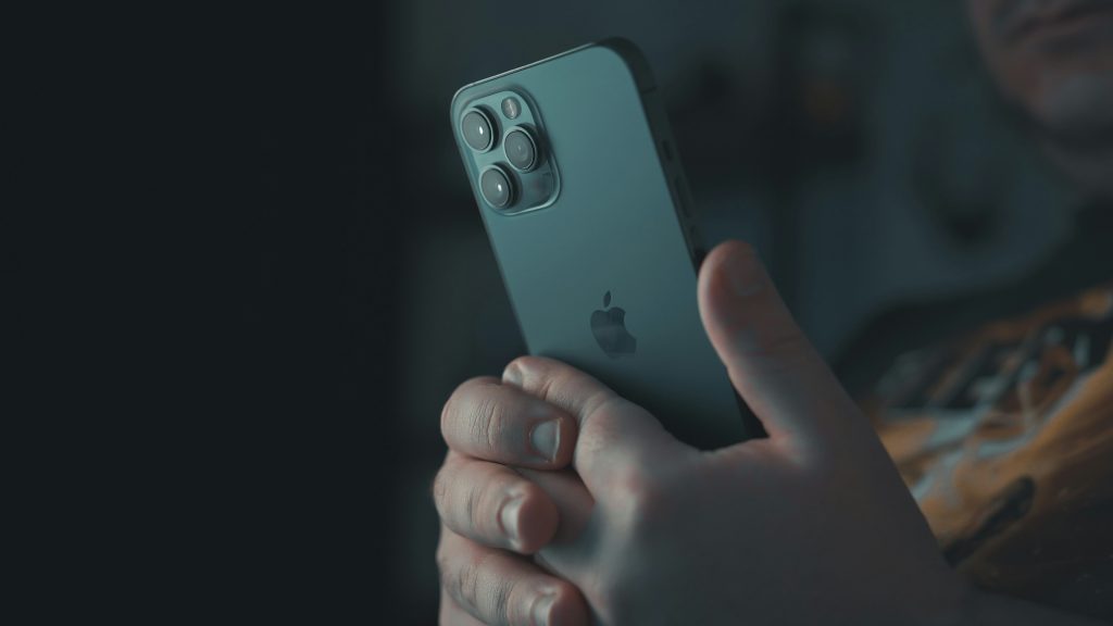 Hand tapping the back of an iPhone demonstrating Back Tap gesture feature, a hidden iOS shortcut for screenshots, flashlight, and quick actions